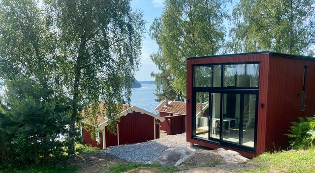 rött modernt attefallshus i sommar miljö med utsikt över vatten en solid dag
