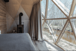 interiör i kupolhus med säng, kamin och stor fönster ut mot naturen