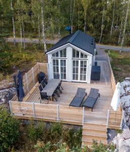 flygbild över attefallshus i sommarmiljö med stor terrass i trä och utemöbler